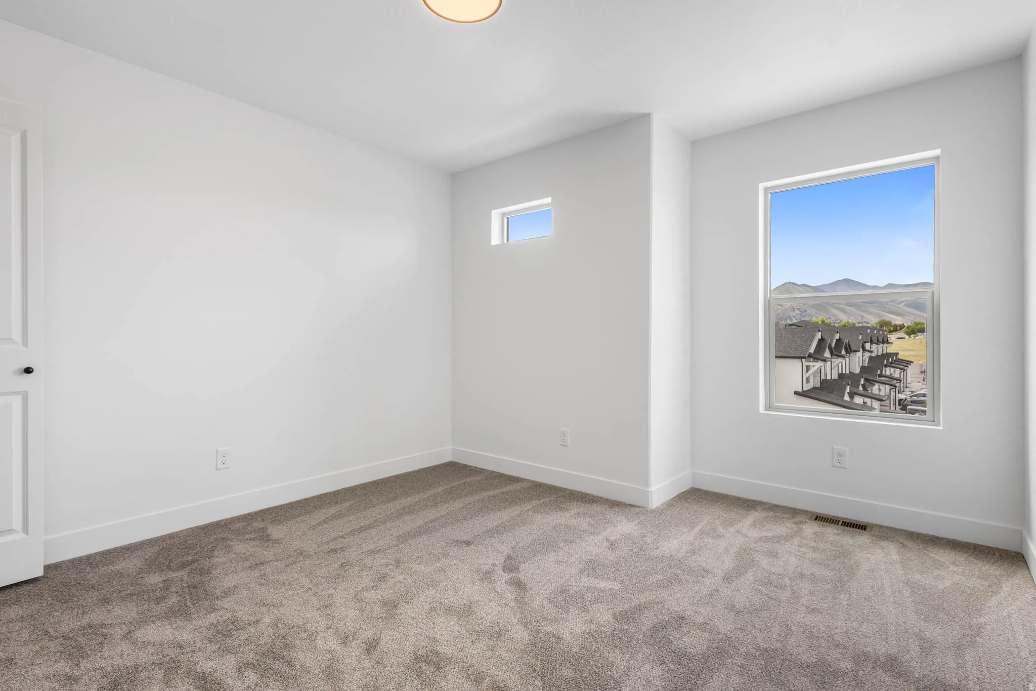Bright room featuring neutral carpeting, white walls, and a large window with mountain scenery