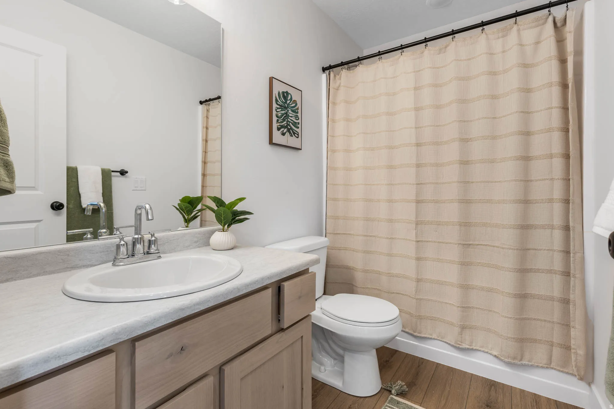 Bathroom featuring a wood-finish floor, light-toned vanity with an integrated sink and chrome faucet, and a toilet
