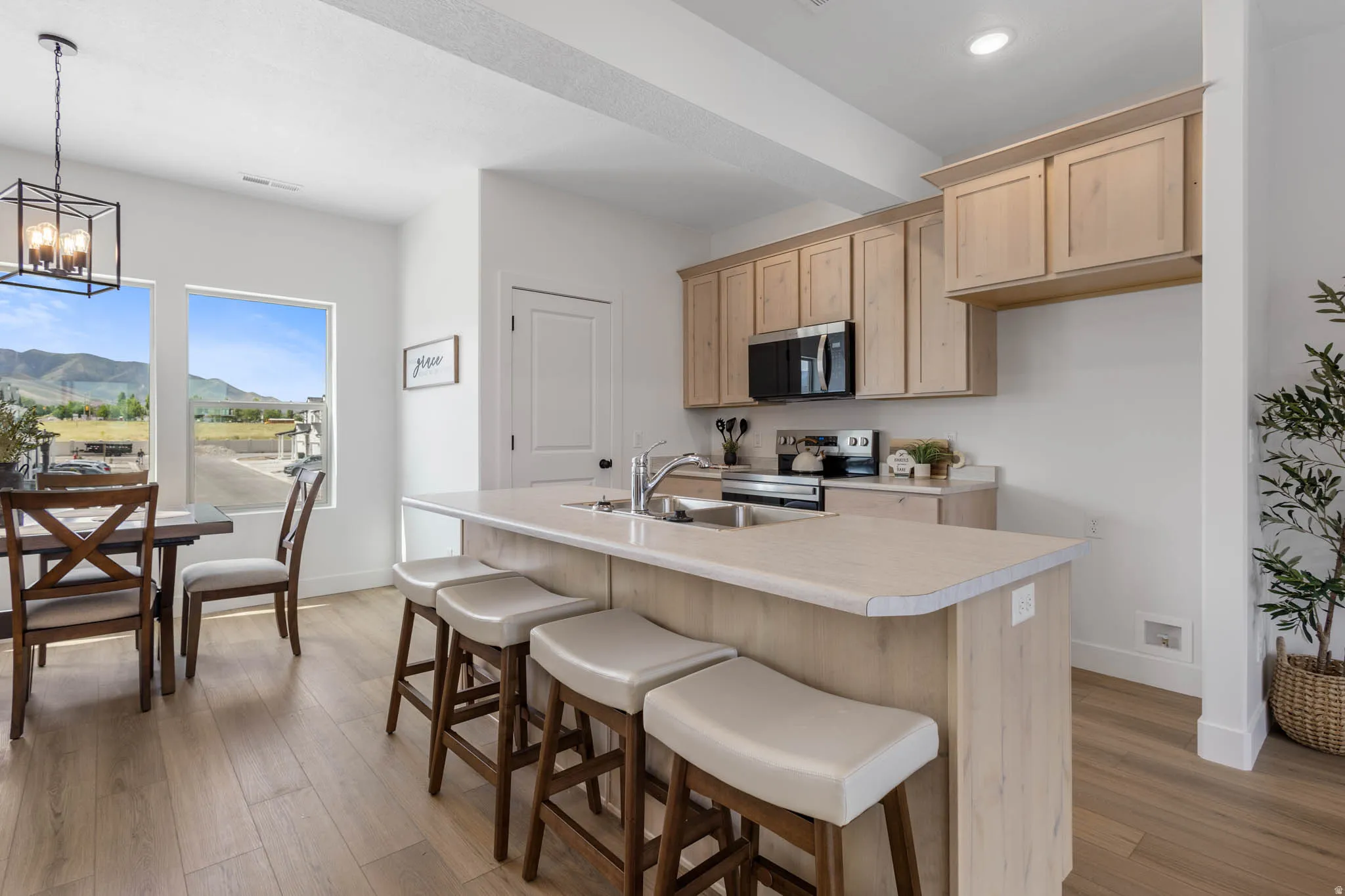 Open-concept kitchen and dining area featuring light wood-finish flooring, a kitchen island with seating, light-toned cabinetry, stainless steel appliances, and large windows