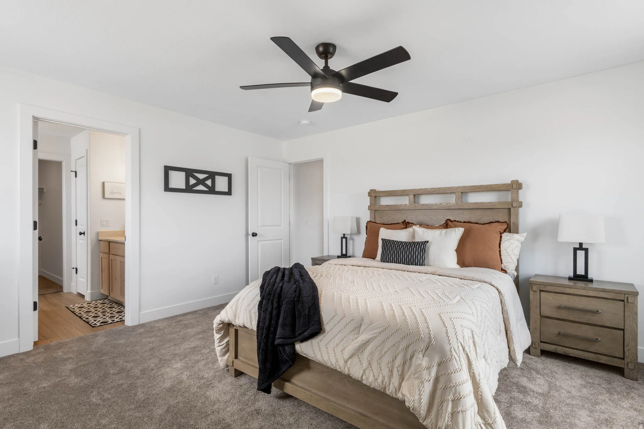 Carpeted bedroom featuring a light wood-finish bed frame and matching nightstands, a contemporary black ceiling fan, and white doors with black hardware