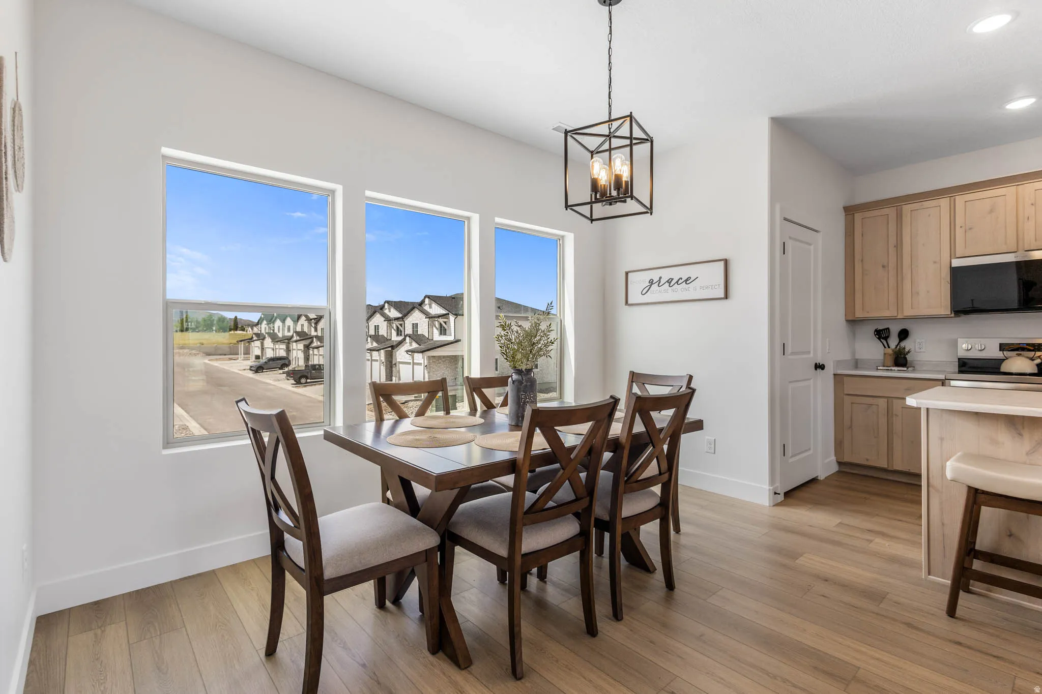 Dining area featuring light wood-finish flooring, a contemporary geometric chandelier, and three large windows
