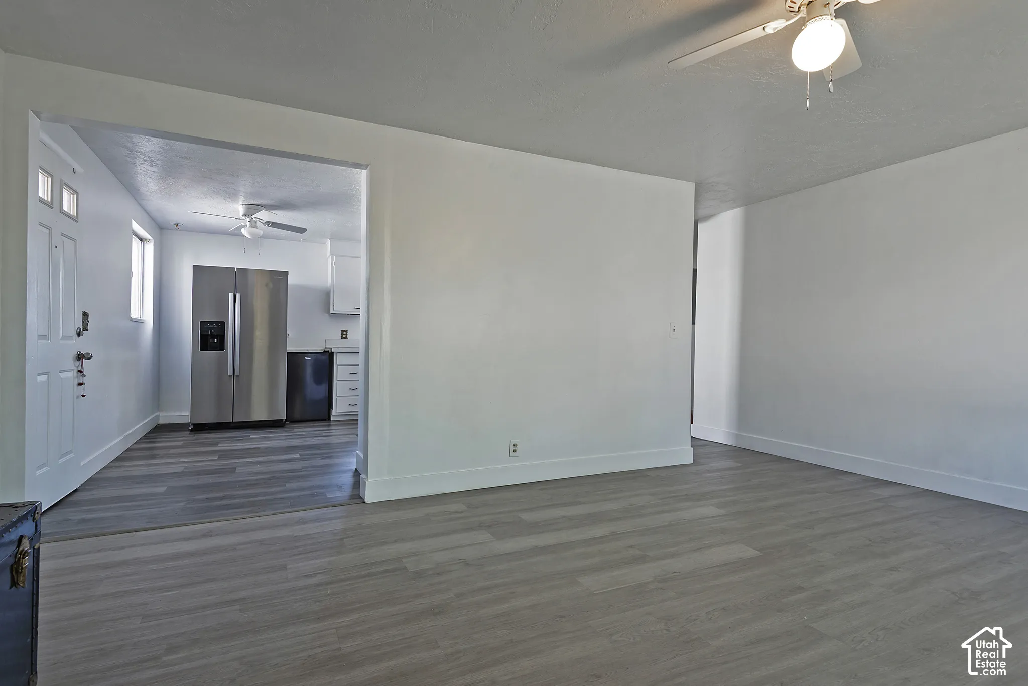 Expansive interior space featuring wood-finish flooring, white baseboards, and a ceiling fan with integrated lighting