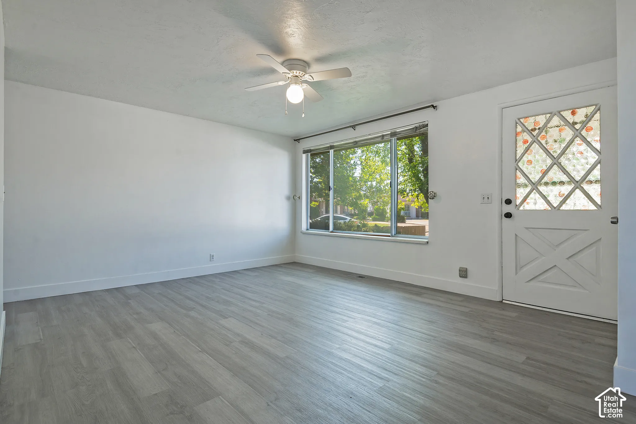 Spacious room featuring wood-finish flooring, a large picture window, and a ceiling fan with integrated lighting