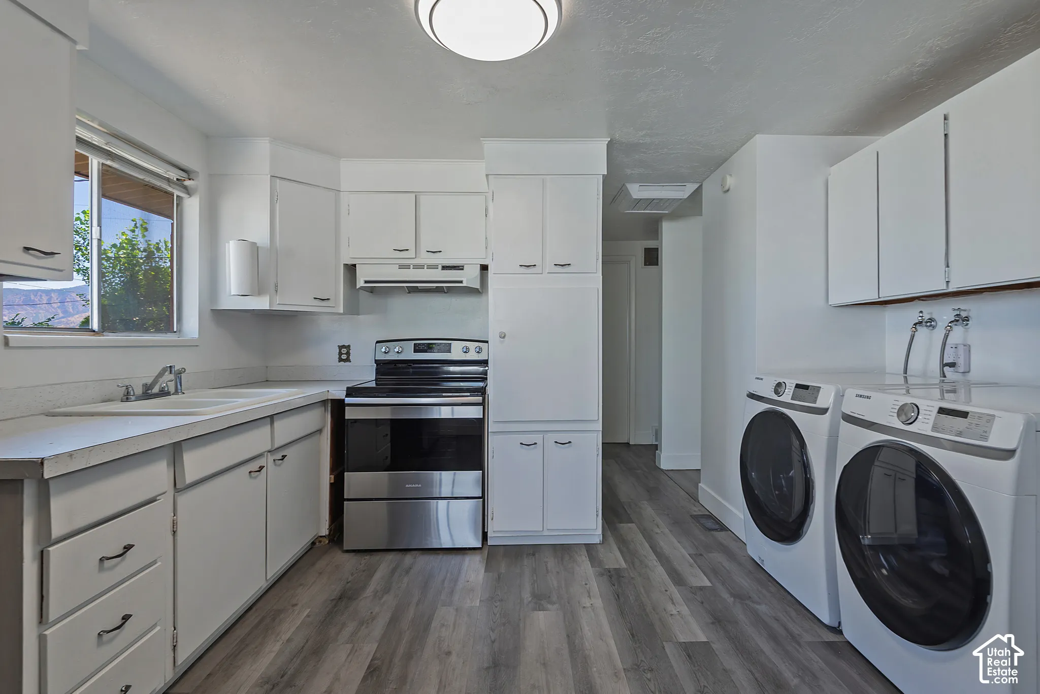 Open-concept kitchen and laundry area featuring wood-finish flooring, white cabinetry with dark pulls, and a stainless steel range