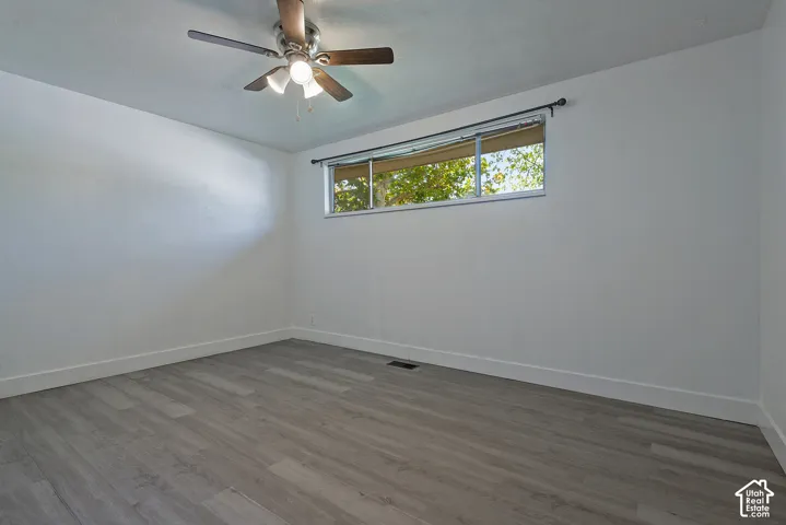 Spacious room featuring wood-finish flooring, a ceiling fan with integrated lighting, and a large window