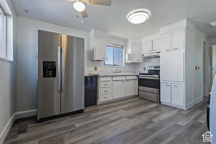 Kitchen featuring wood-finish flooring, white cabinetry, a stainless steel side-by-side refrigerator, a stainless steel range, and a ceiling fan