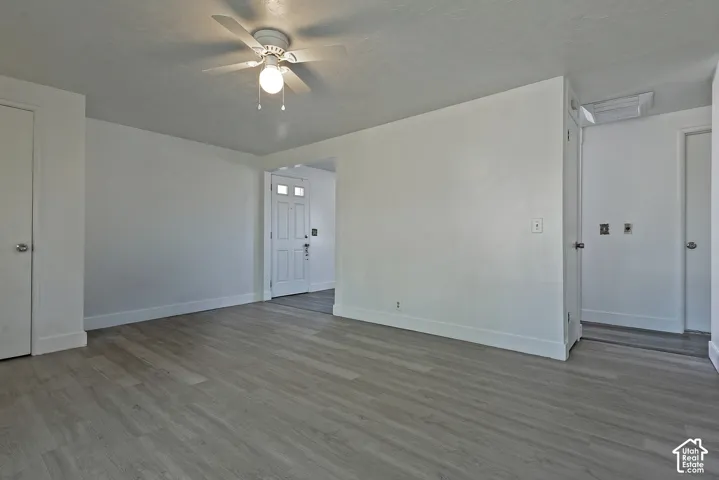 Open living area featuring light wood-finish flooring, white baseboards, and a ceiling fan with integrated lighting