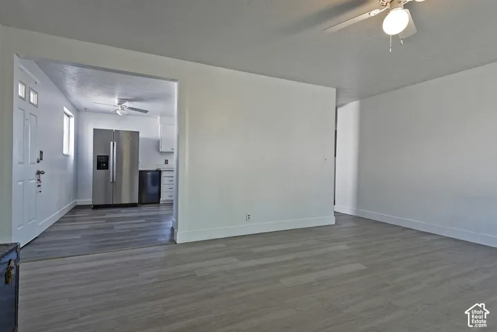 Expansive interior space featuring wood-finish flooring, white baseboards, and a ceiling fan with integrated lighting