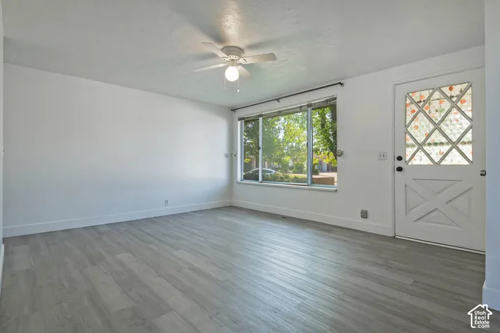 Spacious room featuring wood-finish flooring, a large picture window, and a ceiling fan with integrated lighting