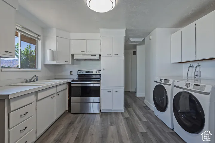 Open-concept kitchen and laundry area featuring wood-finish flooring, white cabinetry with dark pulls, and a stainless steel range