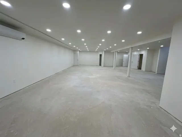 Spacious open-concept area featuring a concrete floor, recessed ceiling lighting, and a wall-mounted climate control unit