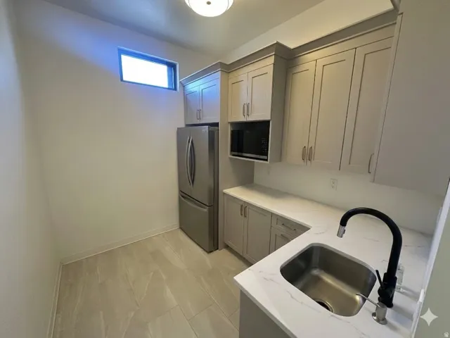 Modern kitchenette featuring light gray shaker cabinetry, stainless steel appliances, white stone countertops, and a single basin sink with a matte black faucet