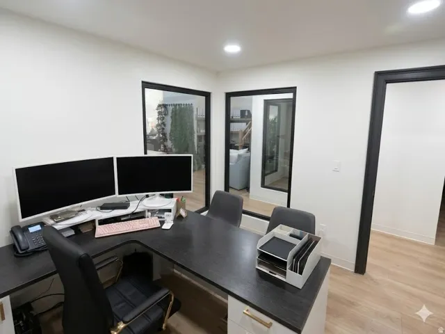 Contemporary office space featuring light wood-finish flooring, recessed lighting, and a white color palette