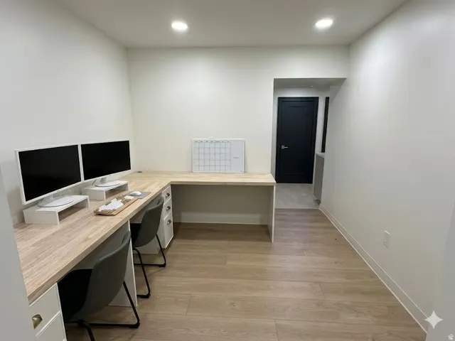 Dedicated workspace featuring an L-shaped built-in desk with a light wood-finish countertop and white cabinetry