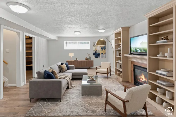Integrated built-in shelving, a fireplace with a wood mantel, wood-finish flooring, a wall-mounted television, and recessed ceiling lighting