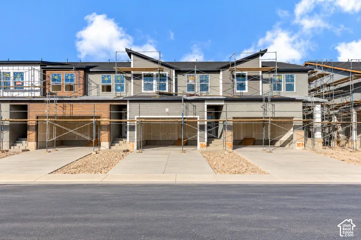 Multi-unit residential structure featuring horizontal lap siding, stone veneer accents, multi-gabled rooflines, and concrete driveways