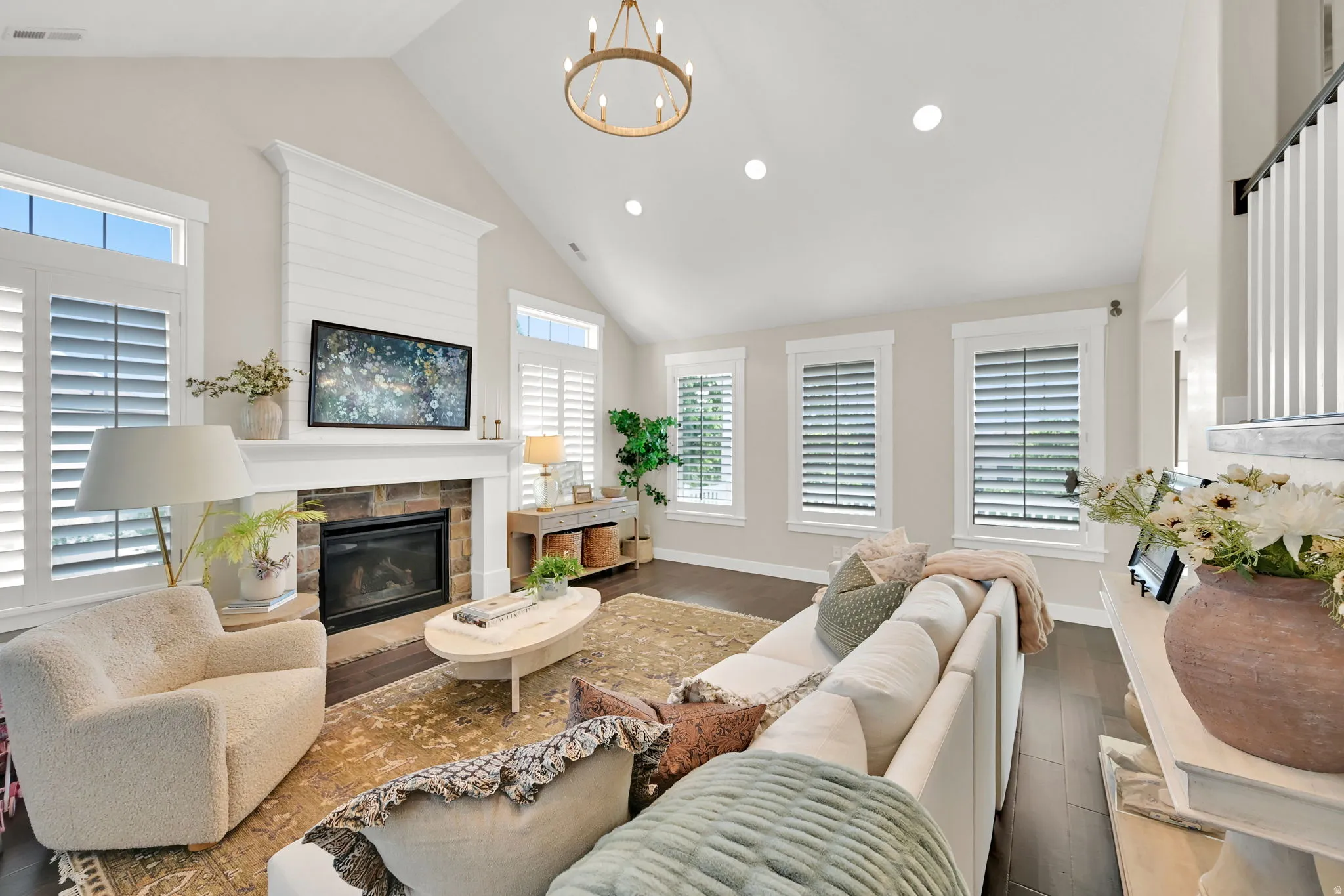 Vaulted ceiling living area featuring a stone fireplace with a shiplap mantel, dark wood-finish flooring, recessed lighting, and a multi-tiered chandelier