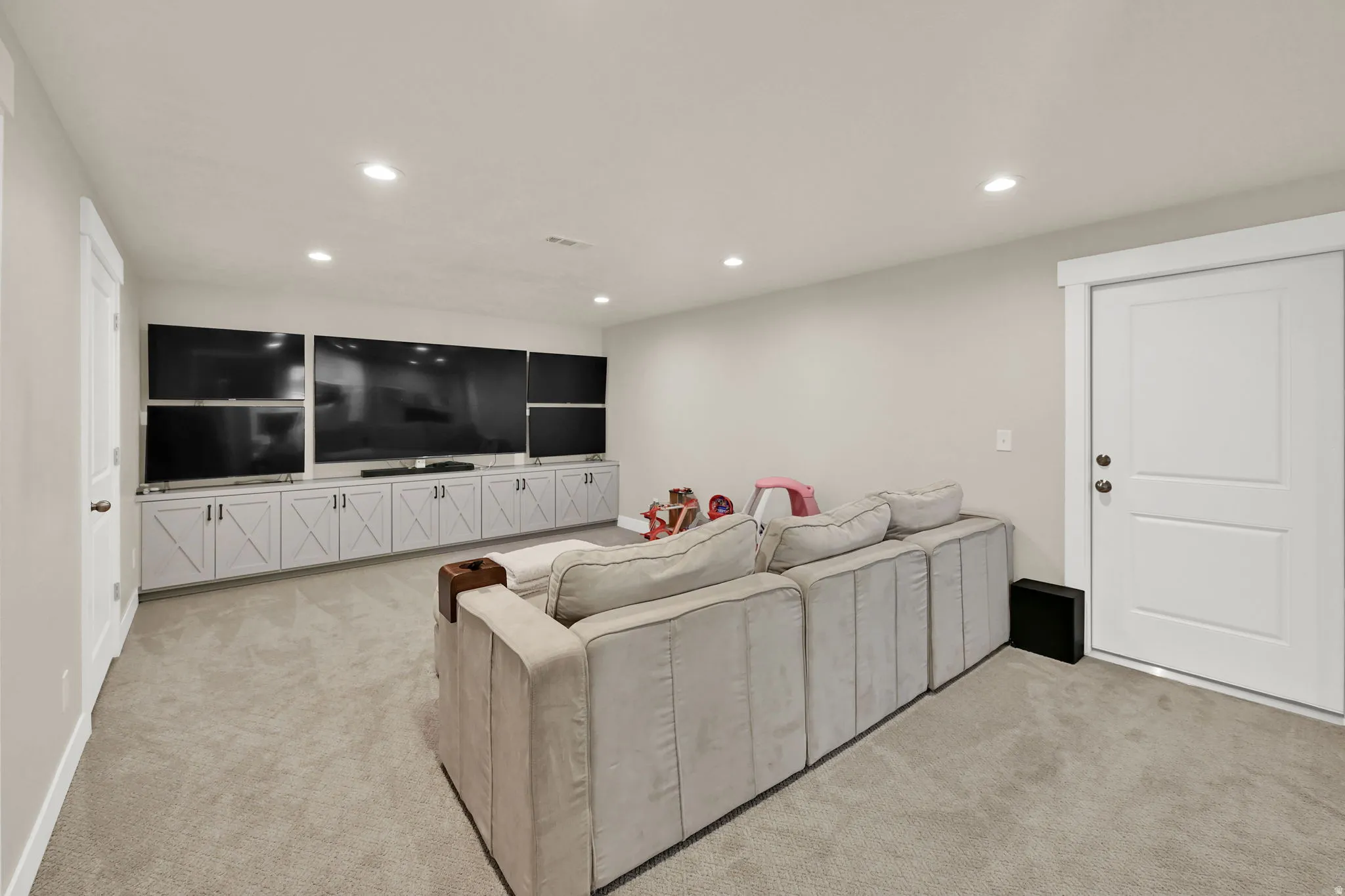 Spacious entertainment room featuring recessed lighting, light-colored carpeting, and a custom media console with barn-door style cabinetry