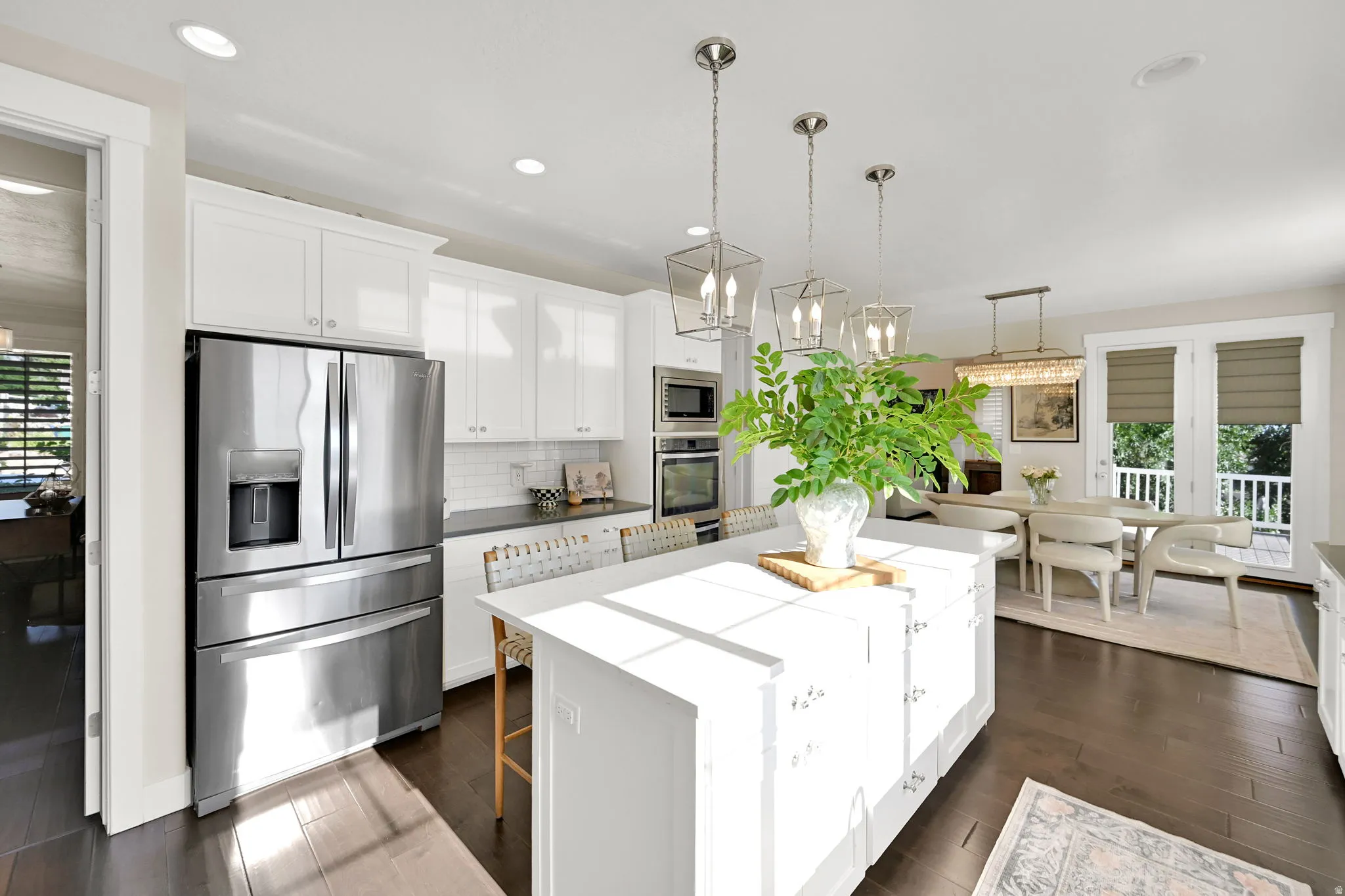 Bright kitchen featuring a substantial island with seating, stainless steel appliances, white cabinetry, dark wood-finish flooring, and pendant lighting