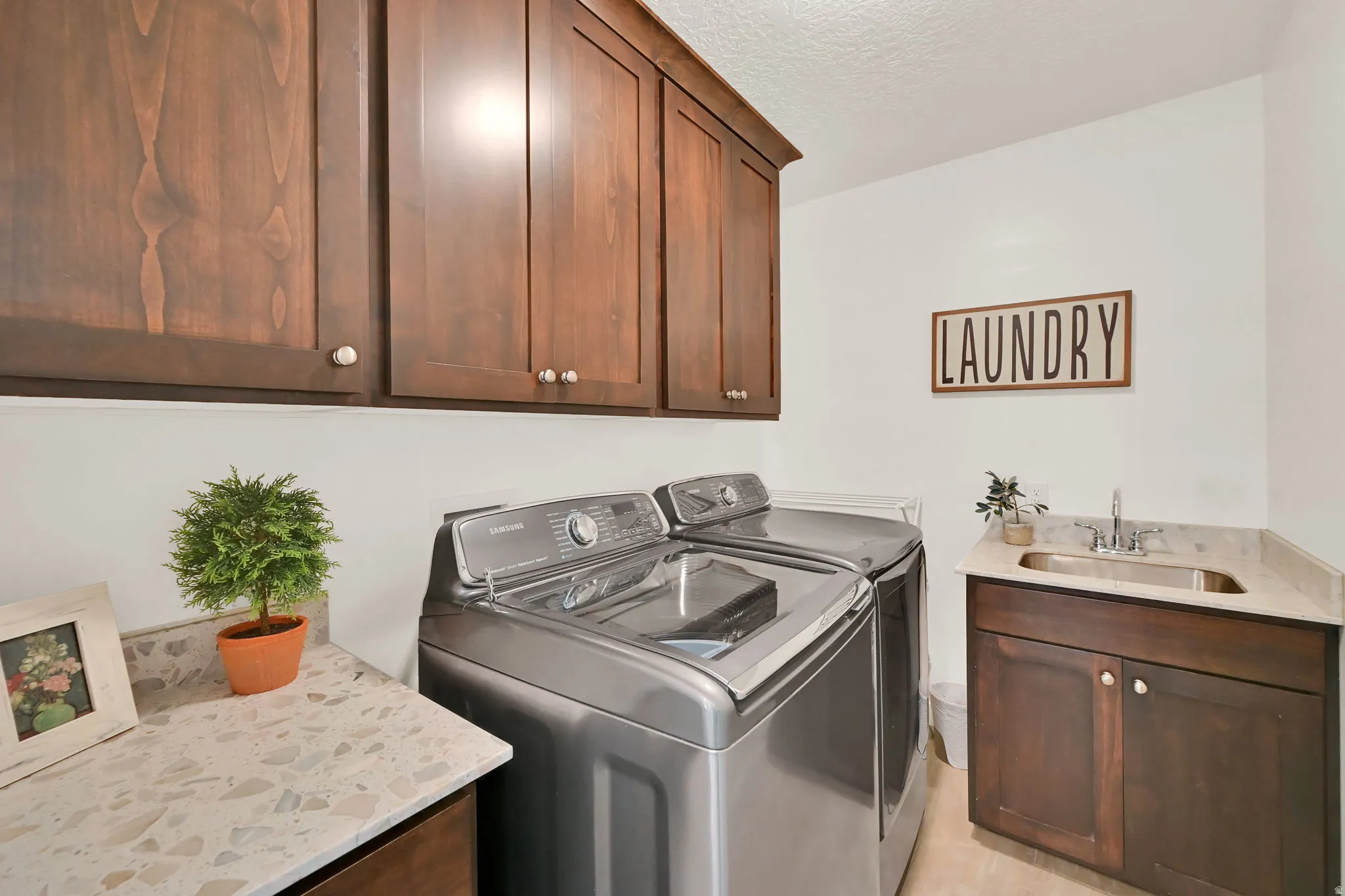 Dedicated laundry area featuring upper and lower cabinetry, a built-in sink with a chrome faucet, light-toned countertops, and light-colored flooring