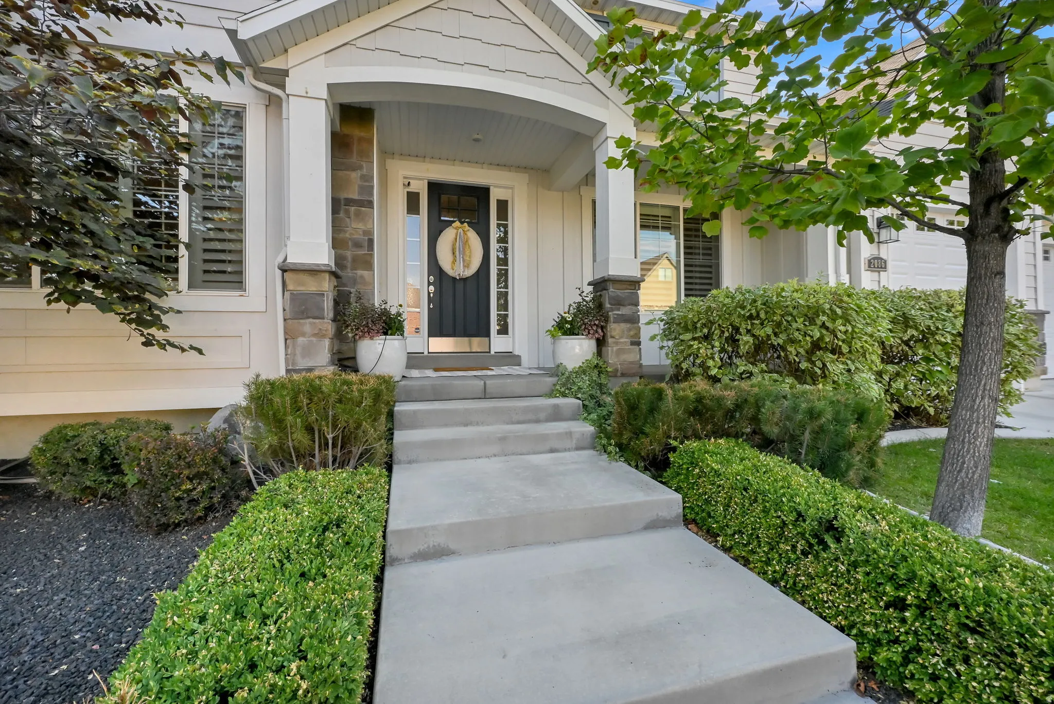 Inviting covered entryway featuring a dark-paneled door with sidelights, stone-clad columns, and a concrete pathway