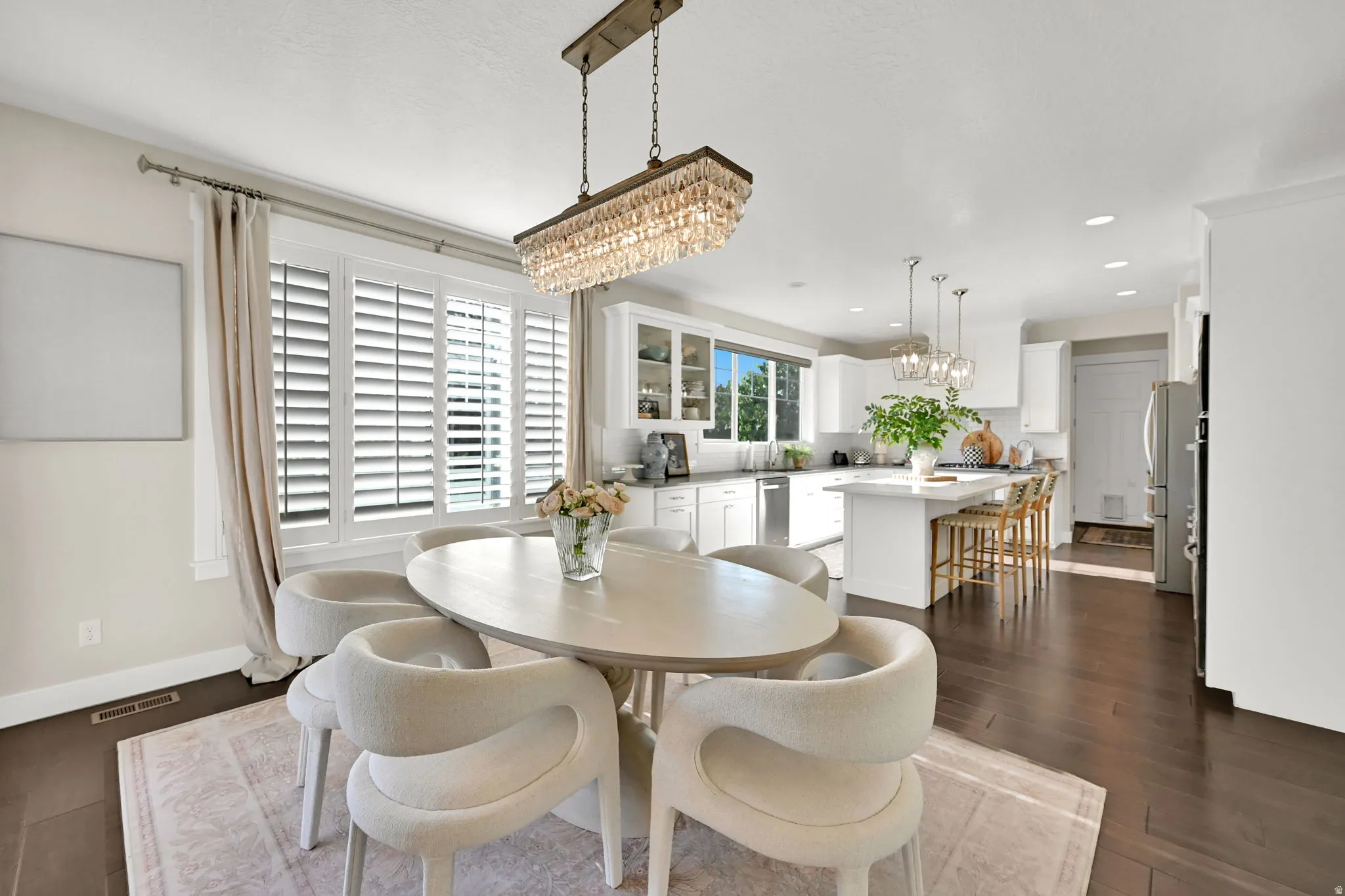 Dining area with an elegant chandelier, wood-finish flooring, and white plantation shutters