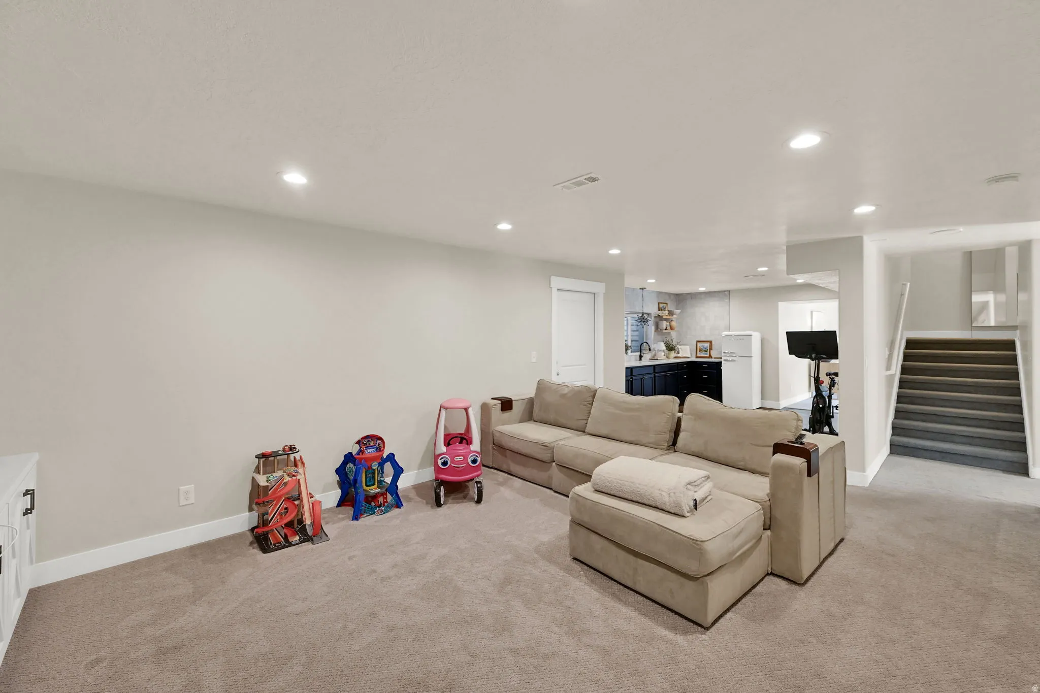 Spacious interior room featuring light gray carpeting, recessed lighting, and white baseboards
