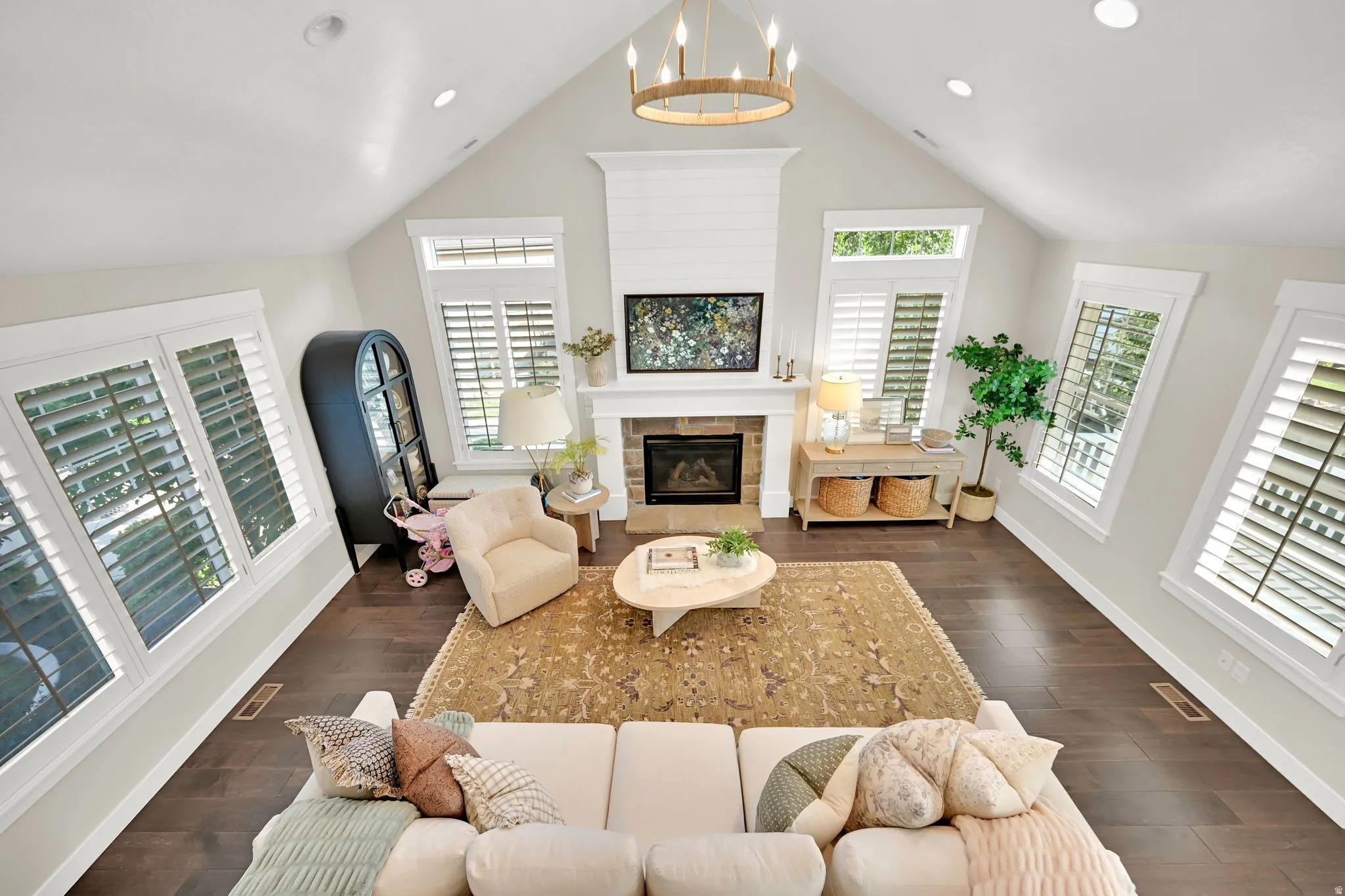 Vaulted ceiling living space featuring dark wood-finish flooring, a shiplap fireplace surround with a stone hearth, and white plantation shutters on multiple windows
