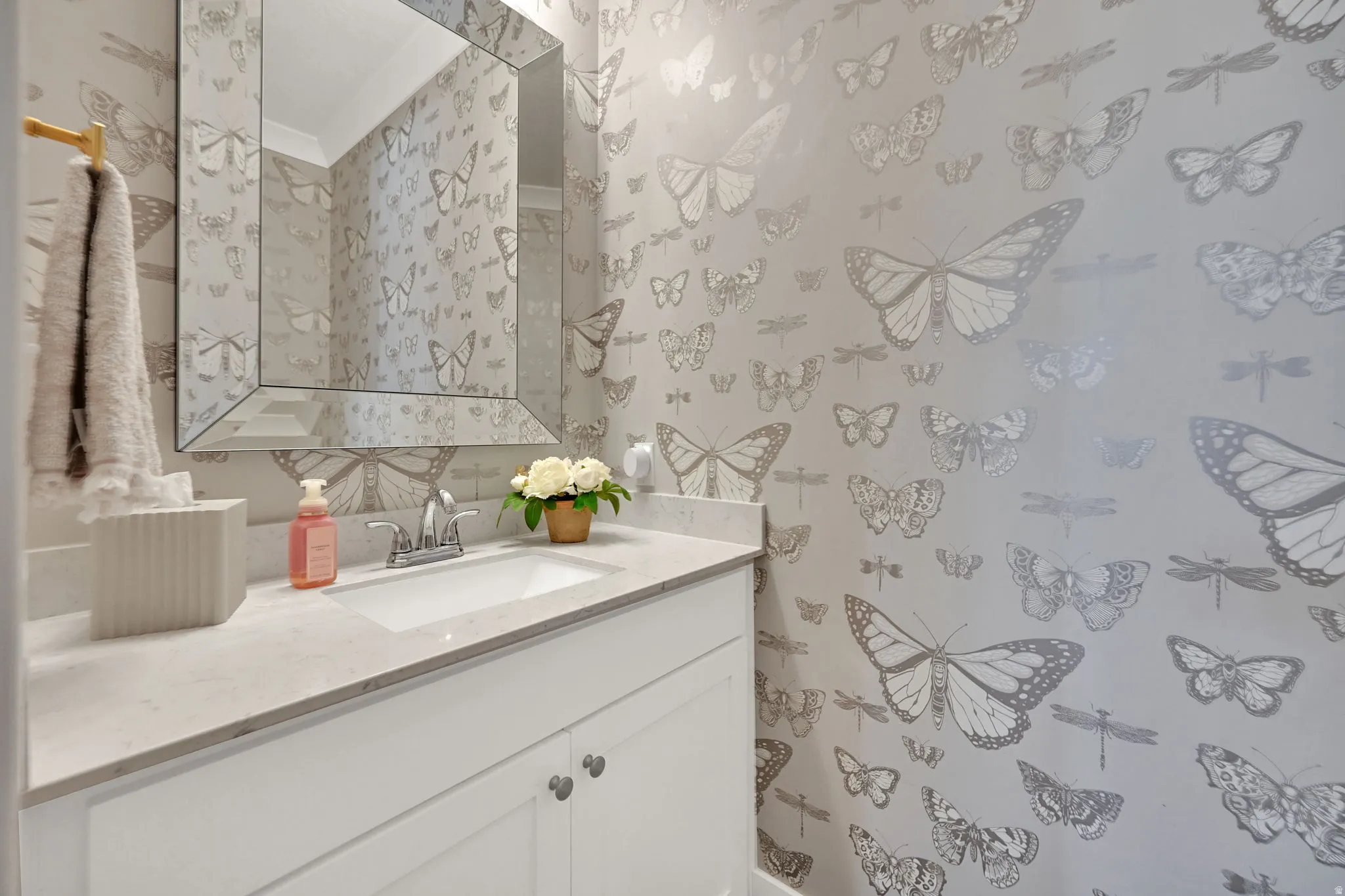 Powder room featuring whimsical butterfly-patterned wallpaper, a white vanity with shaker-style cabinetry, and a light-toned countertop