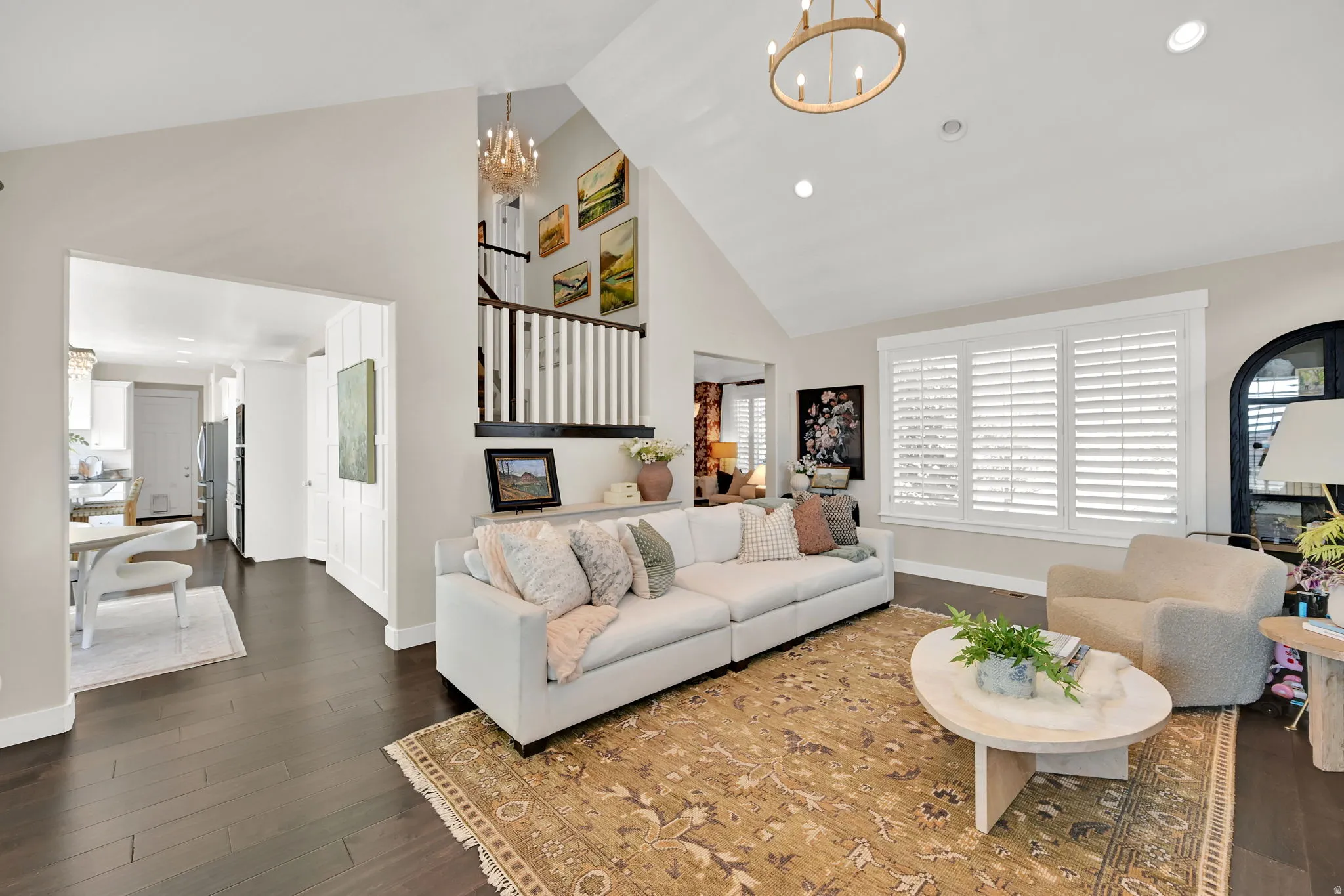 Vaulted ceilings enhance the living space featuring dark wood-finish flooring, recessed lighting, and a prominent window with white plantation shutters