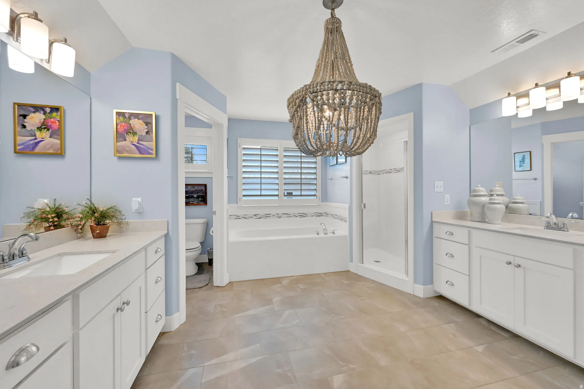 Spacious Primary bathroom featuring a built-in soaking tub, separate shower enclosure, dual vanities with quartz countertops, and a unique beaded chandelier