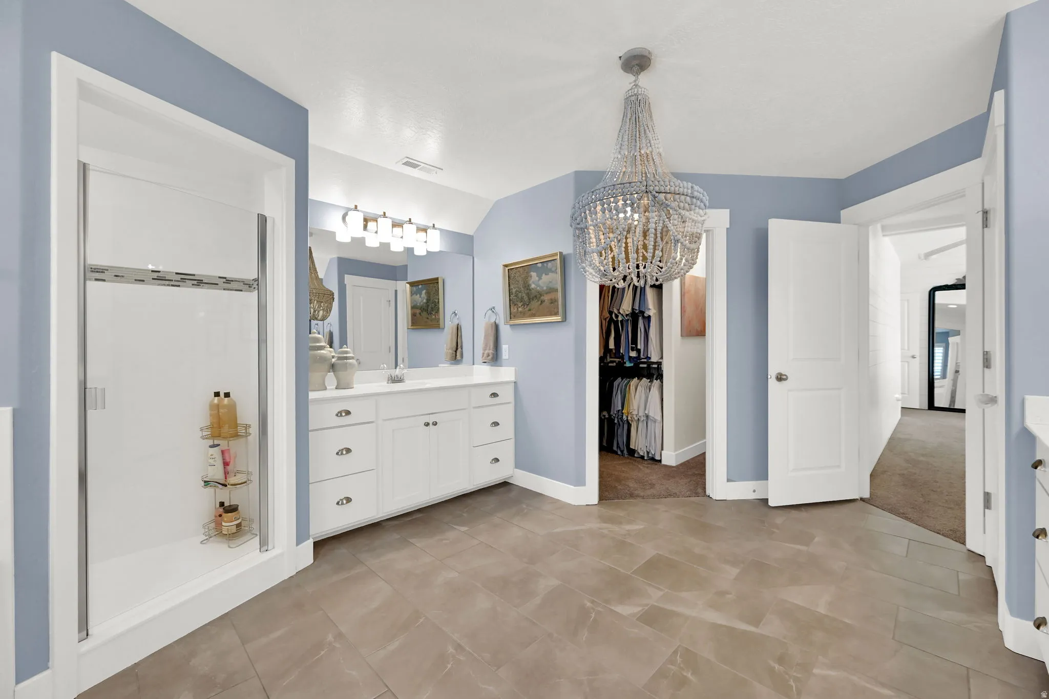 Spacious Primary bathroom featuring a white vanity with double sinks, a walk-in shower with clear glass enclosure, and large format floor tiling
