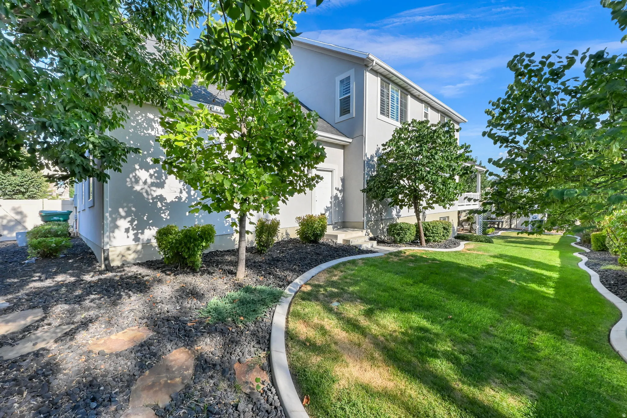 Expansive side yard featuring a lush green lawn, mature trees, and decorative rock landscaping