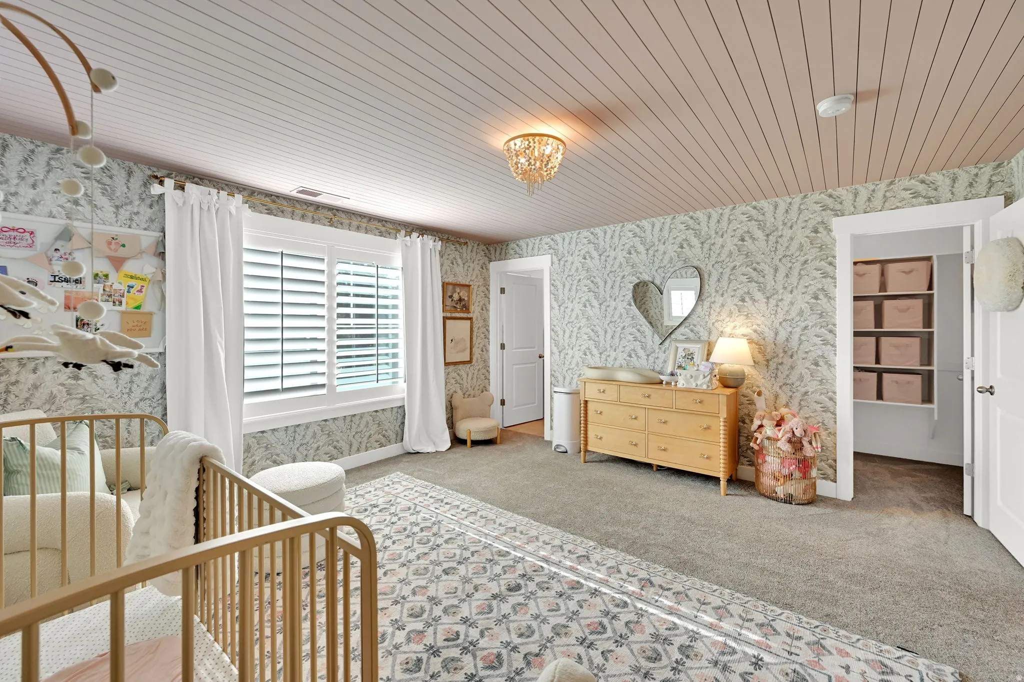Spacious room featuring patterned wallpaper, planked ceiling, and a large window with plantation shutters