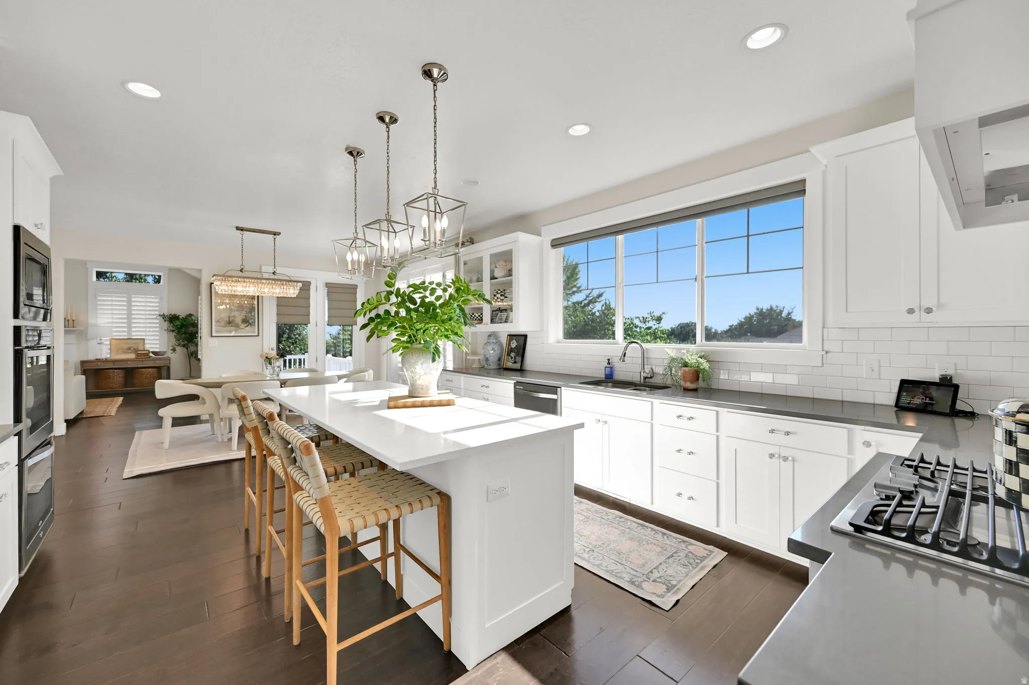 Contemporary kitchen featuring a large central island with seating, dark wood-finish flooring, white cabinetry, dark countertops, and a subway tile backsplash