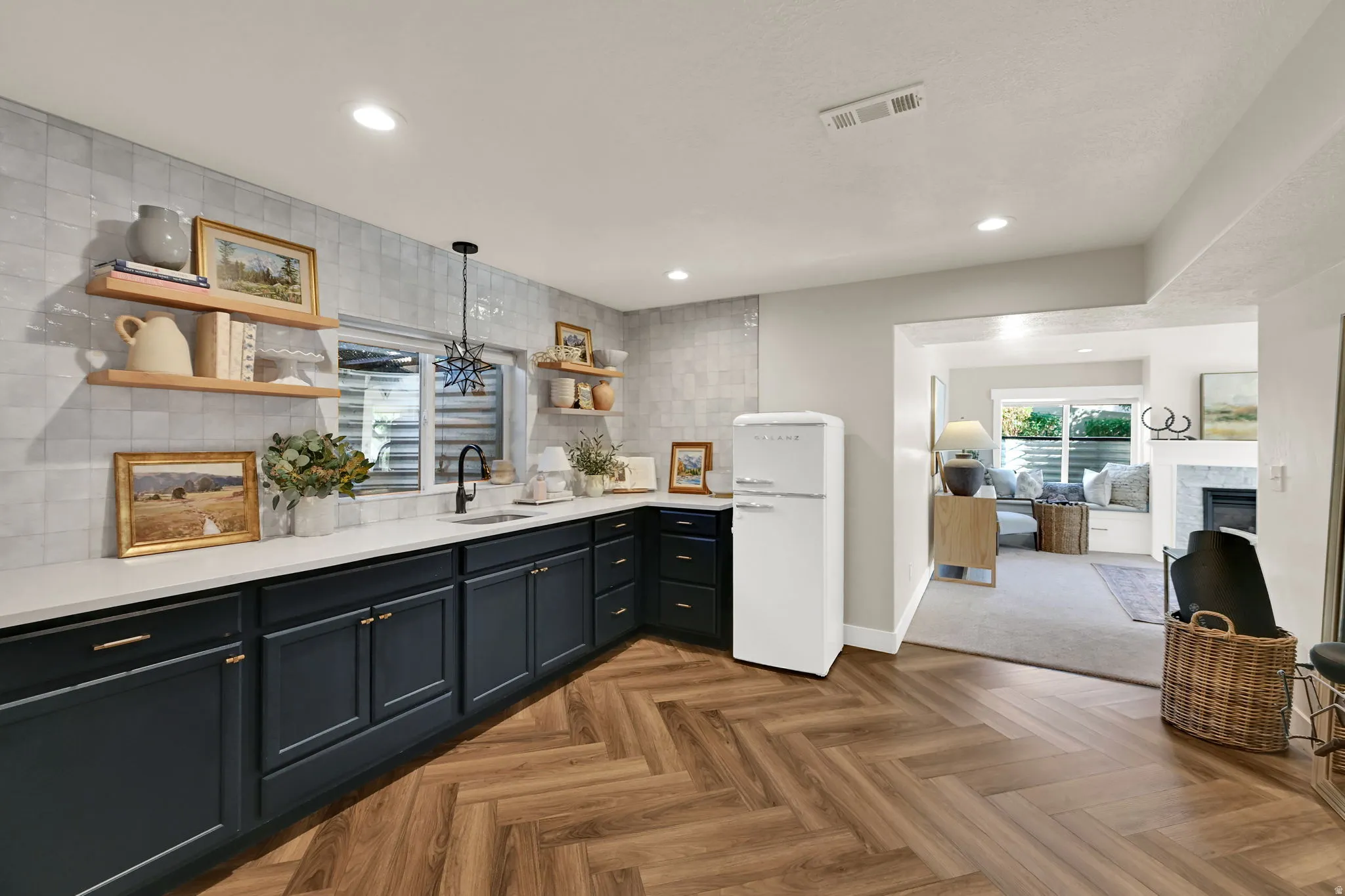 Kitchen featuring wood-finish herringbone flooring, dark cabinetry with gold-tone hardware, white countertops, and light-toned wall tiling