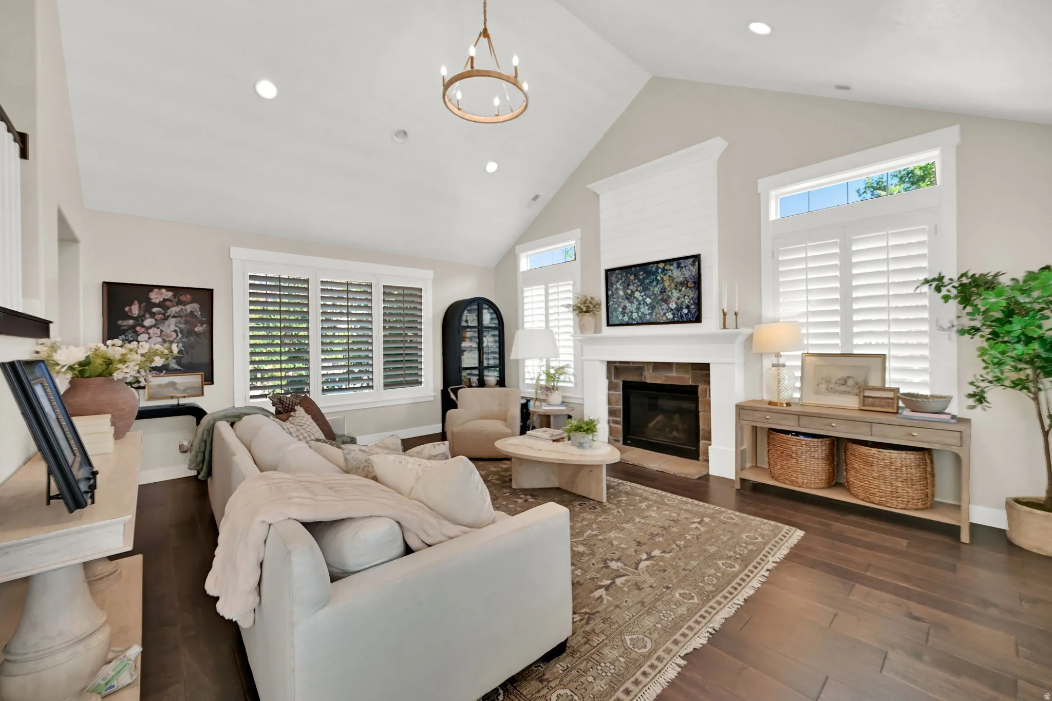 Vaulted ceiling living area featuring a stone surround fireplace with shiplap accent, dark wood-finish flooring, plantation shutters, and recessed lighting