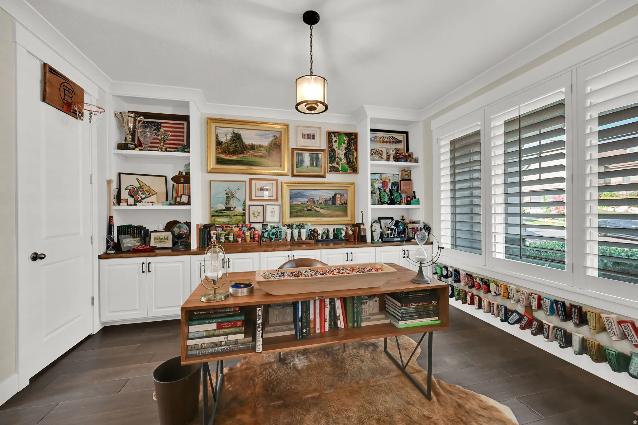 Dedicated space featuring extensive built-in cabinetry, custom shelving, wood-finish flooring, plantation shutters, and a decorative pendant light fixture