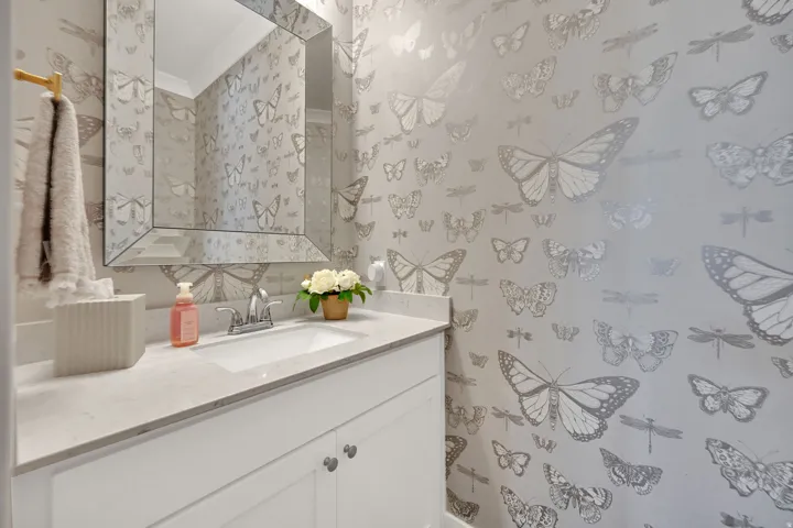Powder room featuring whimsical butterfly-patterned wallpaper, a white vanity with shaker-style cabinetry, and a light-toned countertop