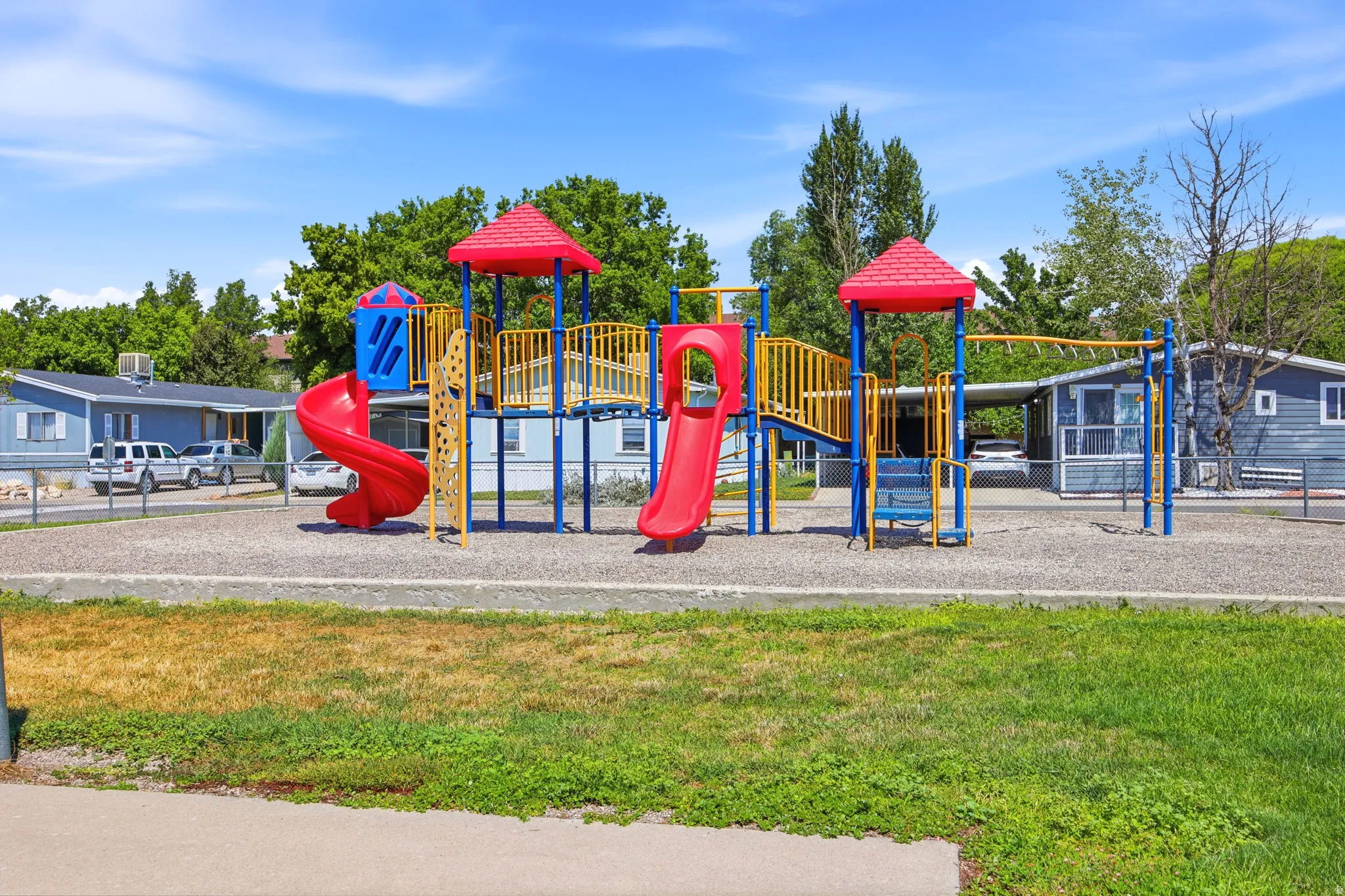 Community playground featuring a multi-level play structure with dual red spiral slides, climbing elements, and covered canopy tops
