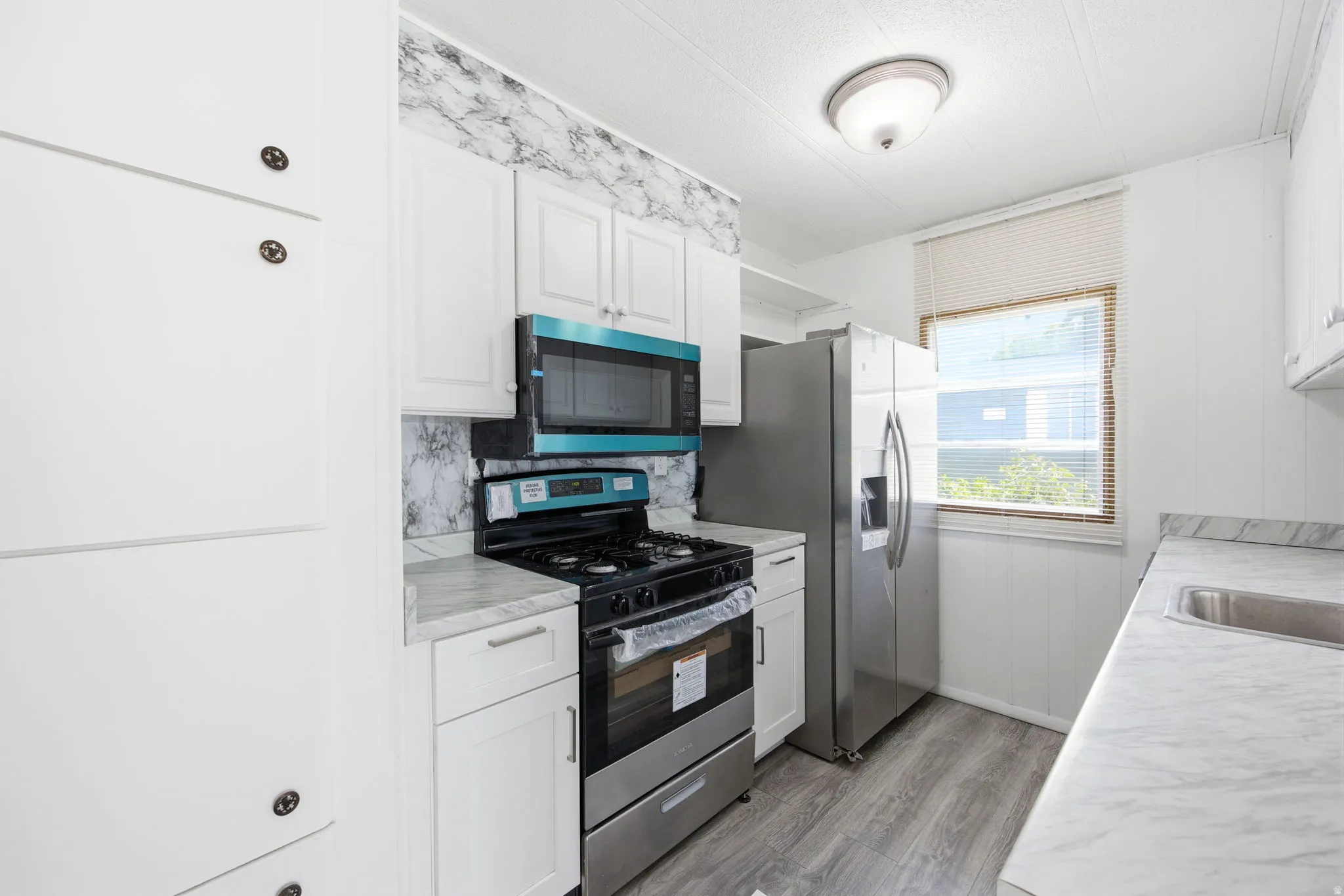Kitchen featuring white cabinetry, gray wood-finish flooring, a stainless steel range with an overhead microwave, and a stainless steel refrigerator