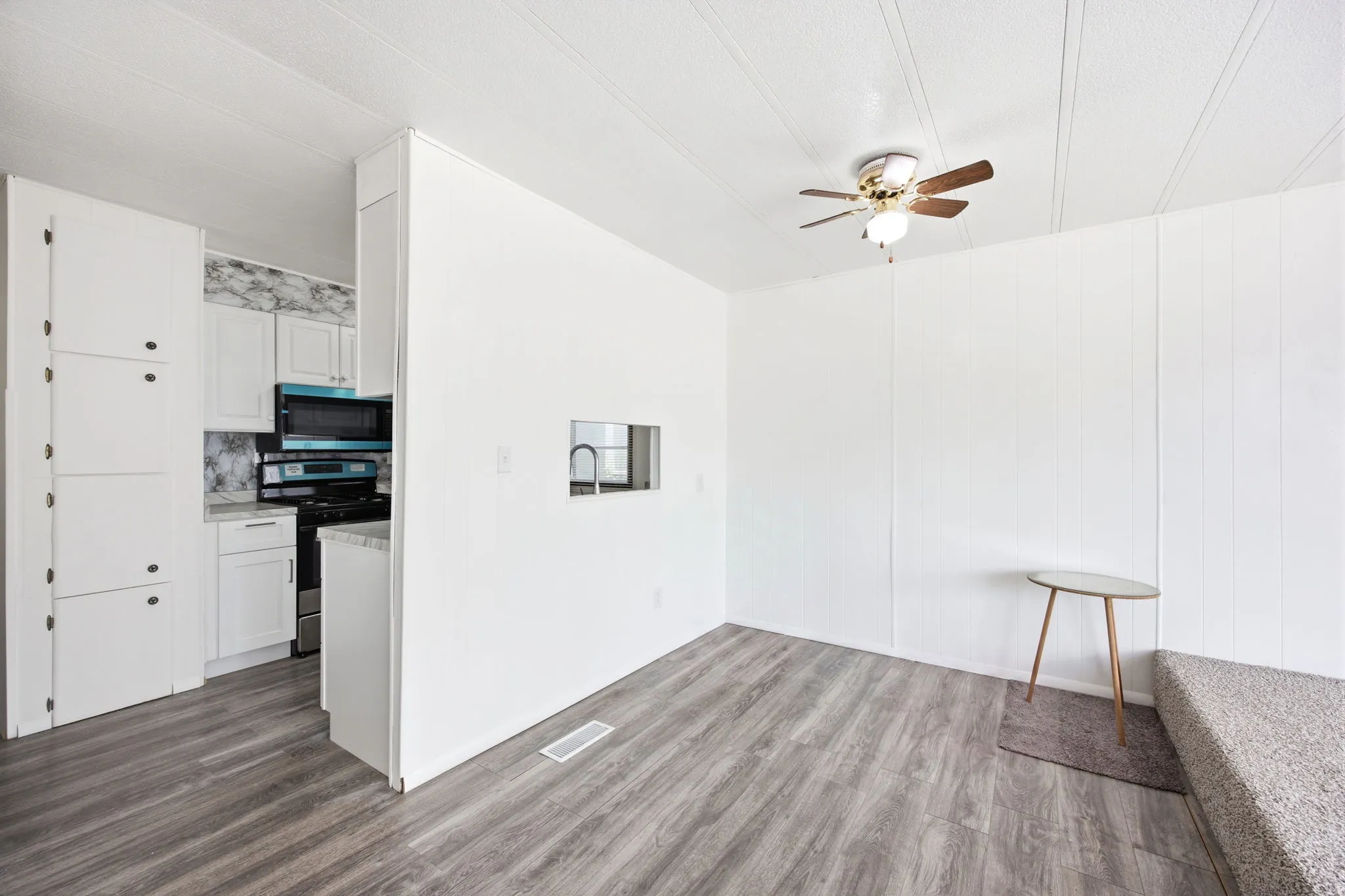 Open-concept living space featuring wood-finish flooring, a ceiling fan, and a pass-through window to the kitchen