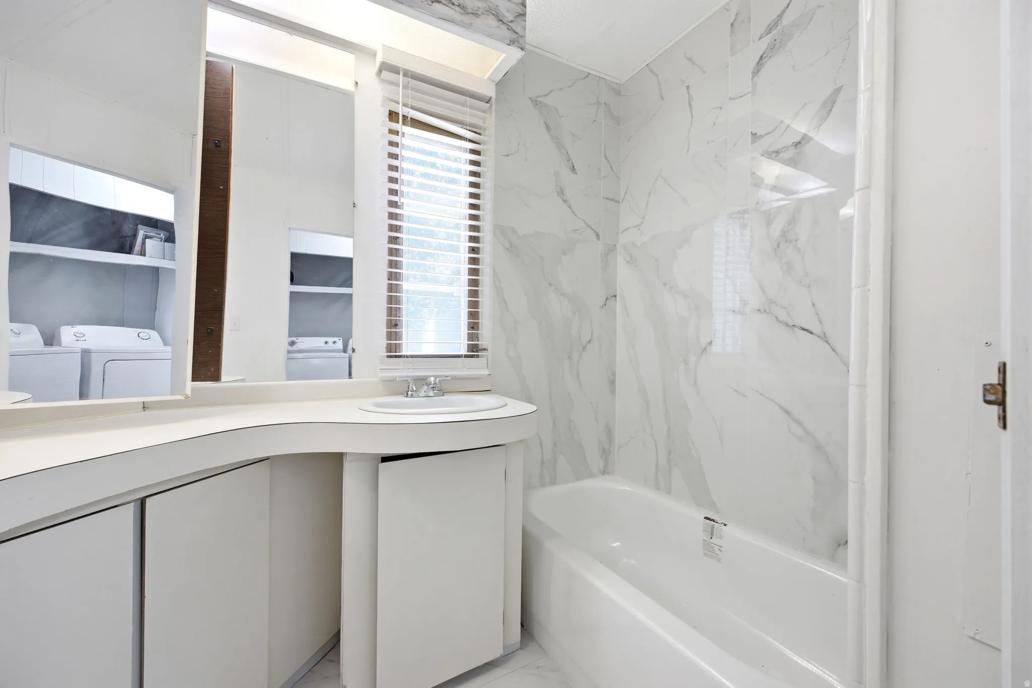 Bathroom featuring a white bathtub, marble-finish wall paneling, a white vanity with integrated sink, and an overhead mirror