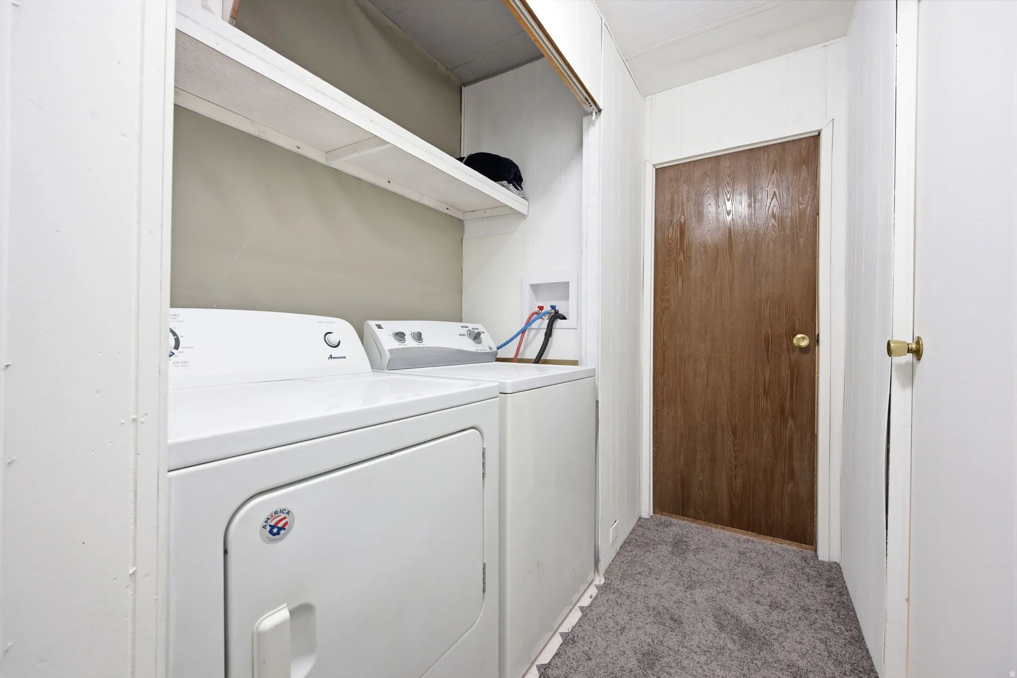 Dedicated laundry area featuring white appliances, a light gray wall, and white upper shelving
