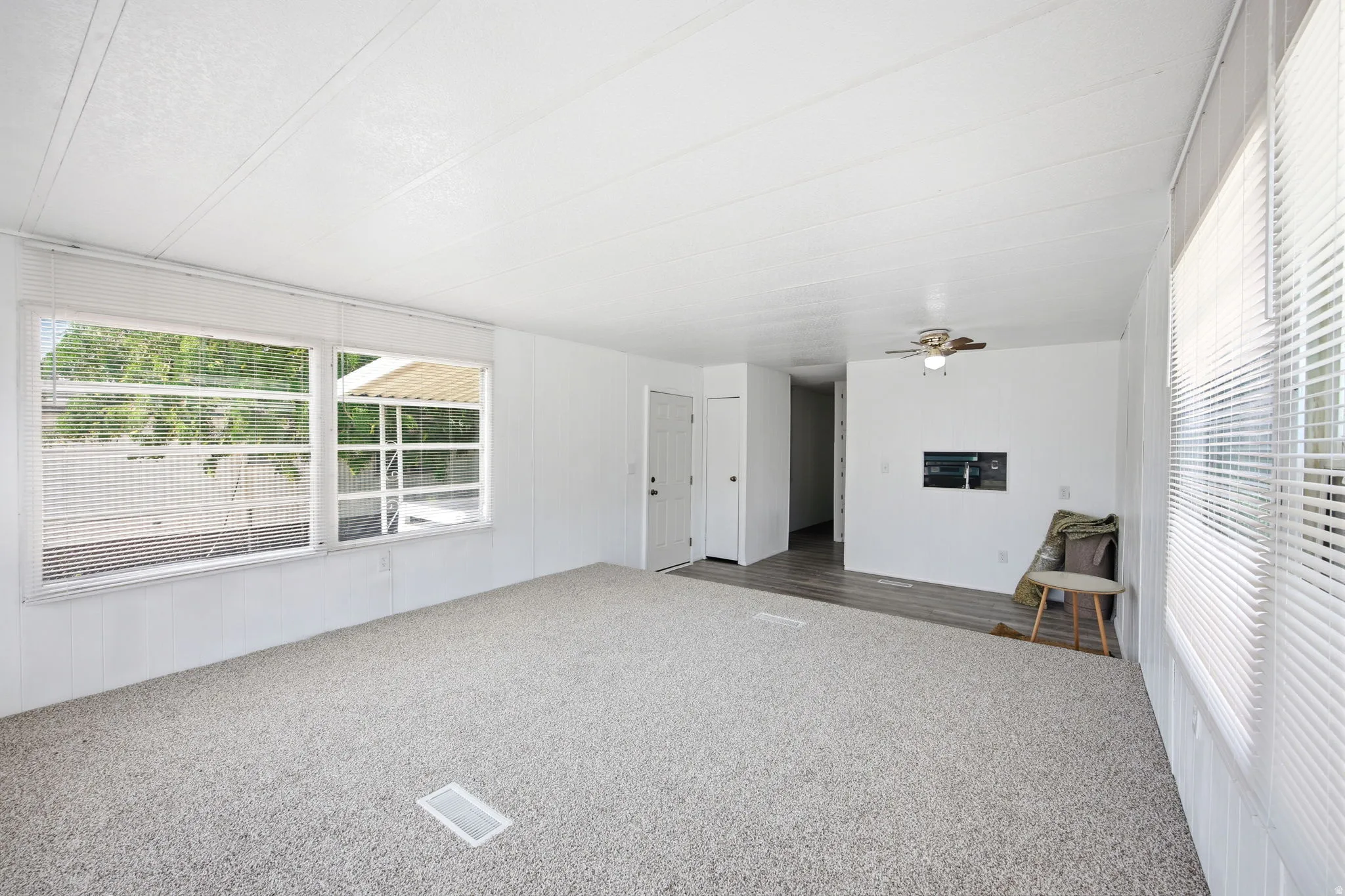 Spacious interior featuring light-toned carpet flooring, multiple windows with horizontal blinds, a white paneled ceiling, and a ceiling fan