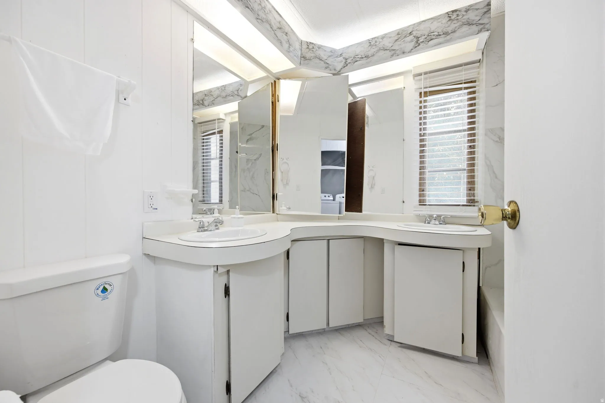 Bathroom featuring a dual vanity with integrated sinks, white cabinetry, and a full mirror wall