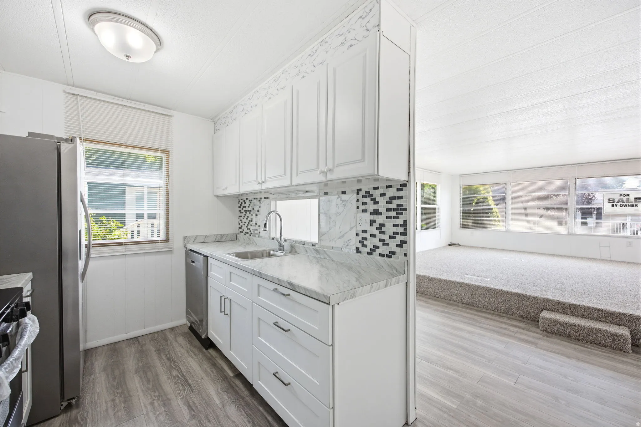 Kitchen featuring white cabinetry, light-toned countertops, a mosaic tile backsplash, and stainless steel appliances