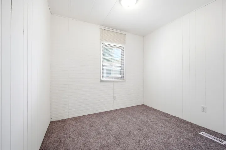 Room with textured white walls, a single window with blinds, and gray carpeting
