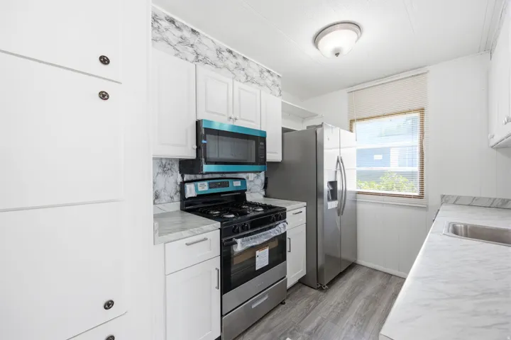 Kitchen featuring white cabinetry, gray wood-finish flooring, a stainless steel range with an overhead microwave, and a stainless steel refrigerator