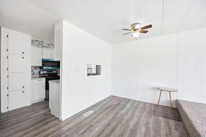 Open-concept living space featuring wood-finish flooring, a ceiling fan, and a pass-through window to the kitchen